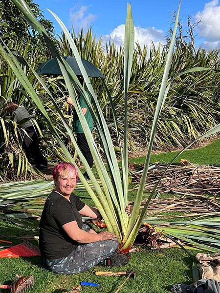 PhD researcher Jaye Barclay cleaning up the pā harakeke at Rātā, holding a large fan of the local cultivar of muka-rich harakeke. Pictured with colleagues who assisted with the mahi. Photo by Kirstine Bruce.